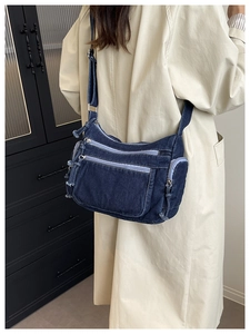 Detail of dark blue denim crossbody bag with multiple zippers and adjustable strap