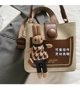 Detail of a beige bucket bag featuring a knit rabbit charm and woven ethnic shoulder strap