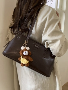 Borsa tote in pelle marrone scuro con ciondolo a forma di orsetto indossata da una modella