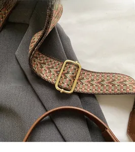 Detail of adjustable woven shoulder strap with gold metal buckle and brown leather