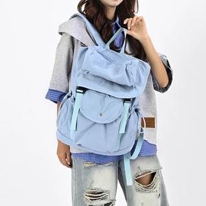 Dettaglio dello zaino in nylon azzurro con fibbia a patta e tasca anteriore sul modello