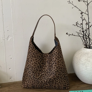 Detailopname van luipaardprint hobo draagtas met bruine leren riem op houten plateau