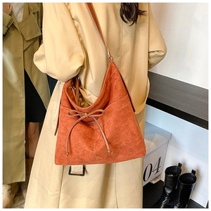 Close-up of orange faux suede tote bag featuring bow drawstring details and chic shoulder strap