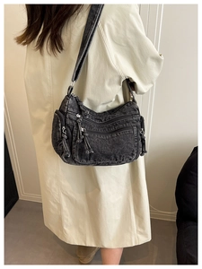 Detail of a black denim crossbody bag with multiple zip pockets and woven zipper pulls