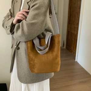 Close-up of brown suede bucket bag featuring a black and white chevron woven strap