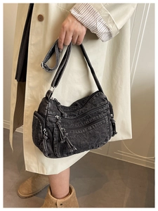 Detail of washed black denim crossbody bag with multi-zipper pockets and rope tassels