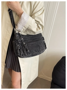 Detail of vintage black denim crossbody bag with multiple zippers and washed texture design