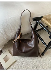 Detail of deep brown hobo bag featuring decorative seam and woven knot charm on white fabric