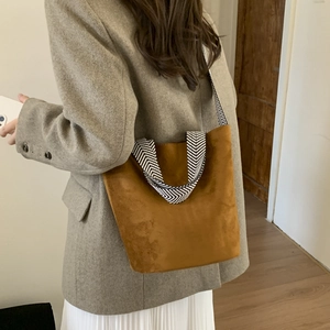 Detailed view of brown suede bucket bag with black and white patterned webbing strap