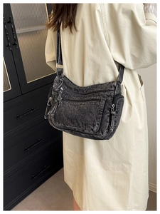 Detail of black washed denim crossbody bag with multiple zippers worn over a beige trench coat