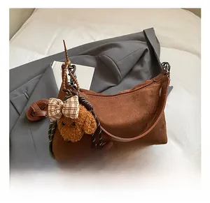 Detail of brown suede crescent bag with a plush puppy charm and red plaid bow
