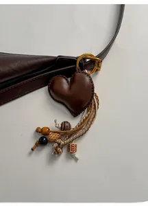 Detail of dark brown leather heart charm with hand-stitched seams and beaded woven ropes