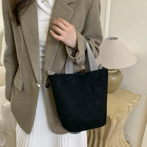 Chic black suede bucket bag featuring a high-contrast black and white woven handle strap