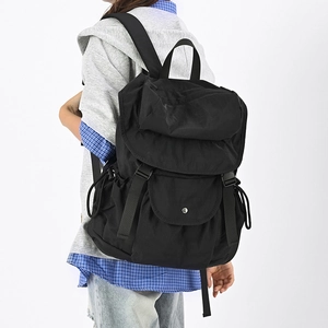 Dettaglio dello zaino in nylon nero con tasca a patta e fibbia indossato da una modella