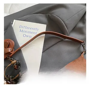 Detailed close-up of brown suede handbag with leather straps and decorative woven charm