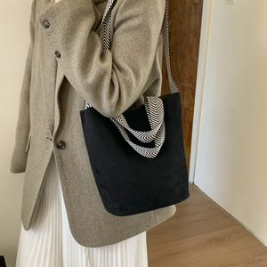 Detail of black suede bucket bag featuring wide black and white herringbone woven strap