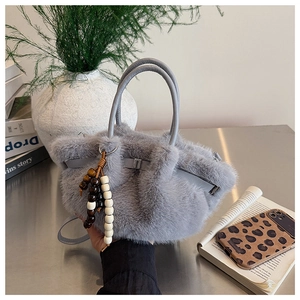 Detail einer grauen Plüschhandtasche mit Holzperlenanhänger auf einer Metallfläche