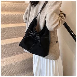 Detail of black suede tote bag with white contrast stitching and bow drawstring detail