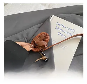 Detail of adjustable brown leather bag strap with metal buckle on a minimalist background