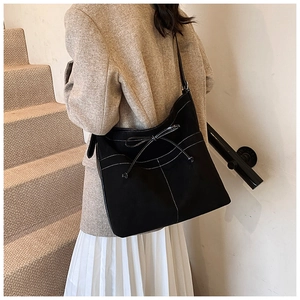 Detail view of black suede tote bag featuring white contrast stitching and bow decoration