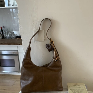 Detailed view of brown leather tote bag with heart charm and woven tassel detail