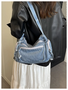 Detail of light blue denim crossbody bag with multiple zippers and wide strap on model