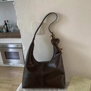 Detail of a dark brown faux leather hobo bag featuring a cute heart-shaped pendant charm
