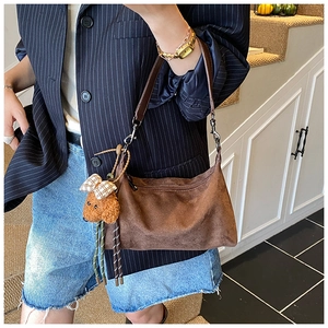 Detailed shot of brown suede shoulder bag with a teddy bear pendant on model