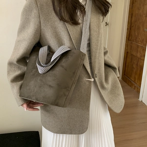 Detail of dark moss green suede bucket bag with wide herringbone fabric strap