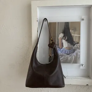 Detail of dark brown hobo bag with vintage texture and heart-shaped pendant accessory