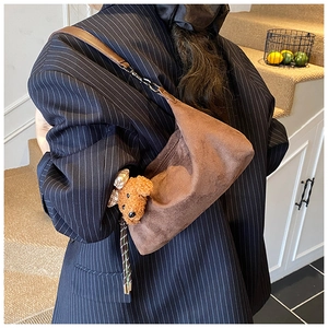 Detail of suede crossbody bag with teddy dog charm on a striped suit model