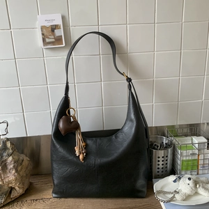 Detail of black hobo tote bag featuring golden buckle and heart bead tassel accessory