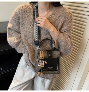 Detail of grey bucket bag with a plaid rabbit charm and herringbone shoulder strap