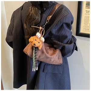 Detail of a brown suede shoulder bag with a cute plush puppy charm on a model's outfit