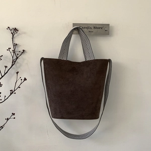 Detail view of coffee suede bucket bag with black and white herringbone woven strap