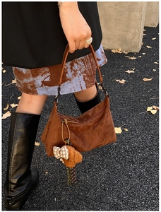 Detail of brown suede tote bag with leather handle and cute bear charm in autumn setting