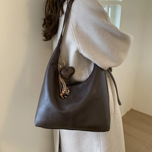 Close-up of deep brown tote bag featuring a leather heart charm and tassel detail