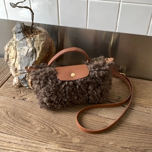 Detail of plush brown shearling bag with faux leather handles and gold metal hardware