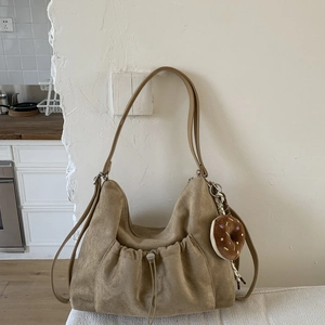 Detalle de bolso tote de ante caqui con bolsillo de cordón y colgante de peluche