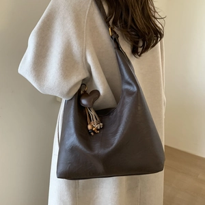 Close-up of dark brown tote bag featuring a leather heart charm and wooden bead tassels