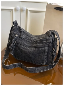Detail of dark grey washed denim crossbody bag featuring multiple metal zipper pockets