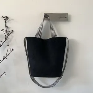 Detail of minimalist black suede bucket bag with black and white chevron woven strap