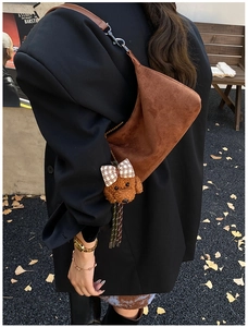 Close-up of a brown suede crescent bag with a cute teddy bear charm in an autumn setting