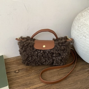 Detail of plush faux fur texture with brown leather flap and golden hardware on handbag