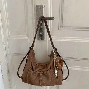 Detalle de bolso de ante marrón con bolsillo de cordón y colgante de felpa decorativo