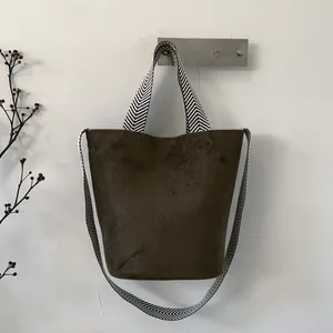 Detail of suede bucket bag in dark brown with geometric patterned jacquard shoulder strap