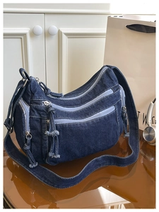 Detailed view of dark denim crossbody bag with multiple zippers and adjustable strap