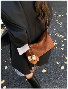 Close-up of brown suede crossbody bag with teddy bear charm on autumn street
