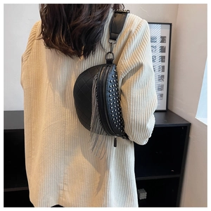 Détail d'un sac demi-lune noir à rivets et pompons sur un élégant blazer beige moderne