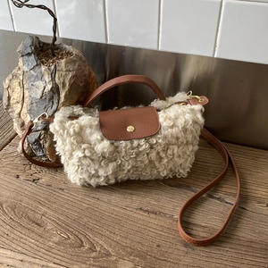 Detail of faux shearling texture and brown leather strap on cream dumpling handbag